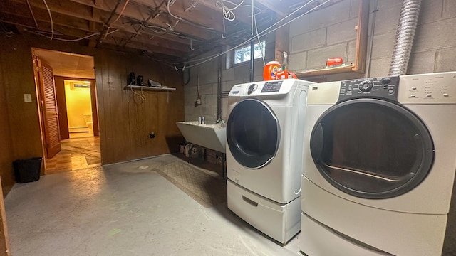 clothes washing area with sink, wooden walls, and washing machine and clothes dryer