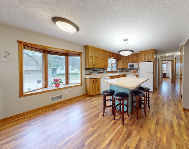 kitchen featuring sink, hanging light fixtures, backsplash, white appliances, and light wood-type flooring