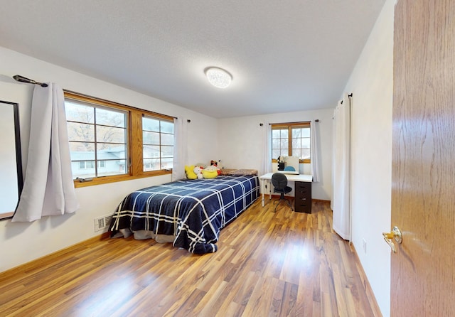 bedroom with a textured ceiling, light wood-type flooring, and built in desk