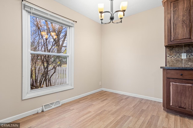 unfurnished dining area with a chandelier and light wood-type flooring