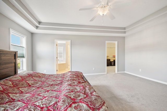 bedroom with ensuite bath, light colored carpet, ceiling fan, a tray ceiling, and a spacious closet