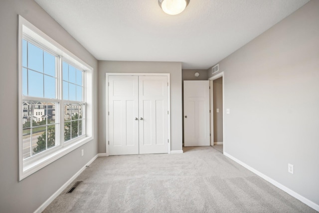 unfurnished bedroom with light colored carpet and a closet