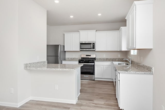 kitchen with appliances with stainless steel finishes, light wood-type flooring, light stone counters, sink, and white cabinets