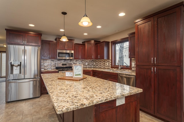 kitchen with light stone counters, stainless steel appliances, sink, a kitchen island, and hanging light fixtures