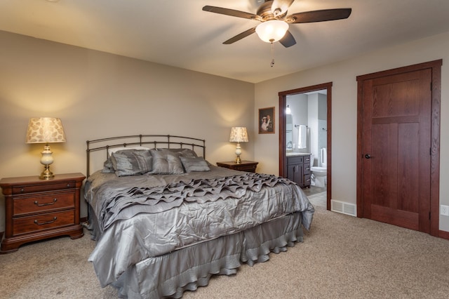 bedroom with ceiling fan, light colored carpet, and ensuite bath