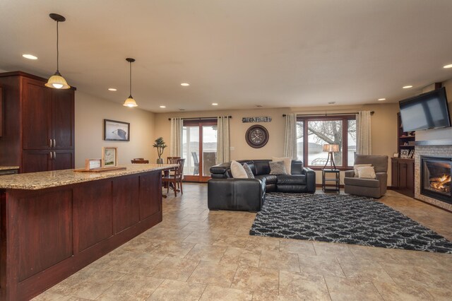 24539 Twilight Ln, Pelican Rapids, MN 56572 - kitchen featuring light stone finish floors, a glass covered fireplace, light stone counters, open floor plan, and hanging light fixtures
