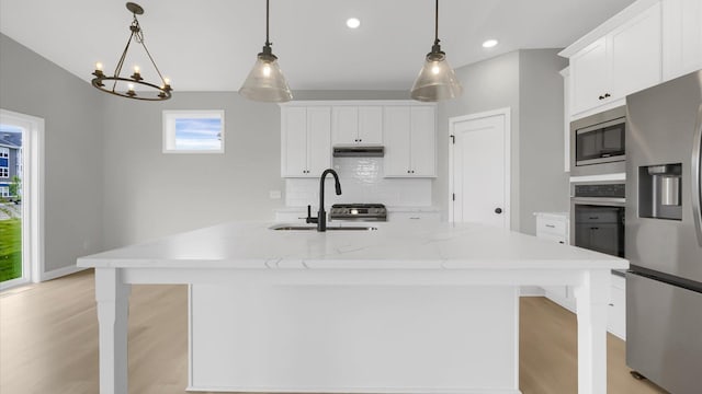 kitchen with stainless steel appliances, a kitchen island with sink, white cabinetry, and pendant lighting