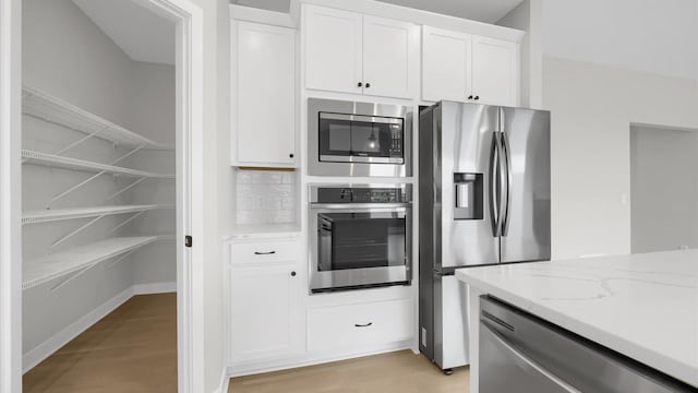 kitchen featuring white cabinets, light stone countertops, light wood-type flooring, and appliances with stainless steel finishes