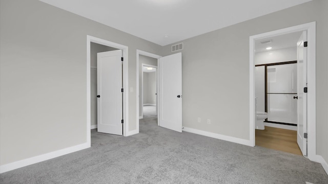 unfurnished bedroom with ensuite bathroom, light colored carpet, and a spacious closet