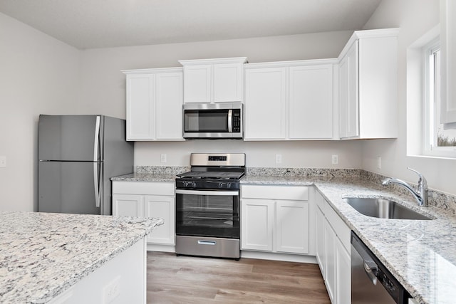 kitchen with light hardwood / wood-style floors, stainless steel appliances, white cabinets, sink, and light stone countertops