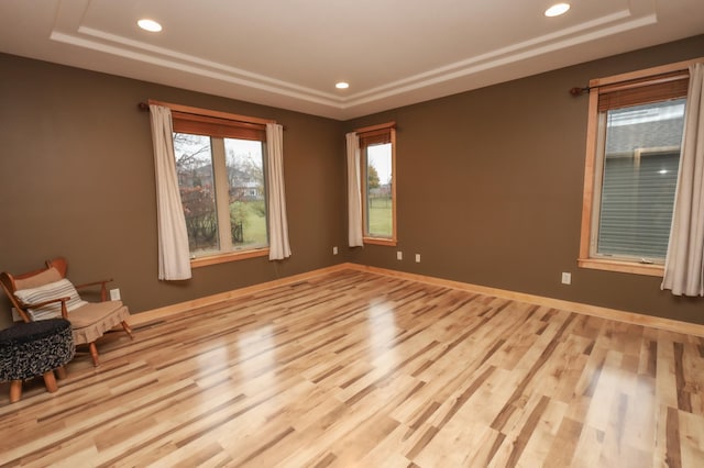 spare room with a tray ceiling and light wood-type flooring