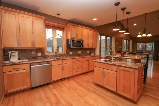 kitchen featuring appliances with stainless steel finishes, a center island with sink, pendant lighting, and a healthy amount of sunlight