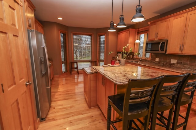 kitchen with backsplash, light hardwood / wood-style flooring, appliances with stainless steel finishes, decorative light fixtures, and a kitchen bar