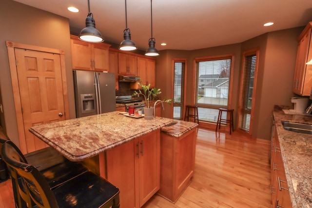 kitchen featuring appliances with stainless steel finishes, light hardwood / wood-style floors, a kitchen island, and light stone counters