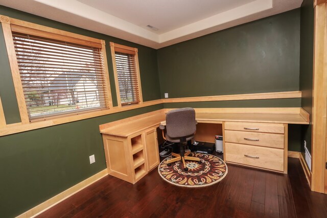 office space with built in desk, a raised ceiling, and dark wood-type flooring