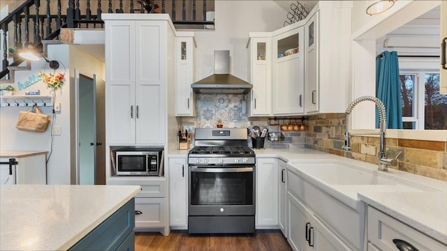 kitchen featuring white cabinets, wall chimney range hood, appliances with stainless steel finishes, tasteful backsplash, and dark hardwood / wood-style flooring