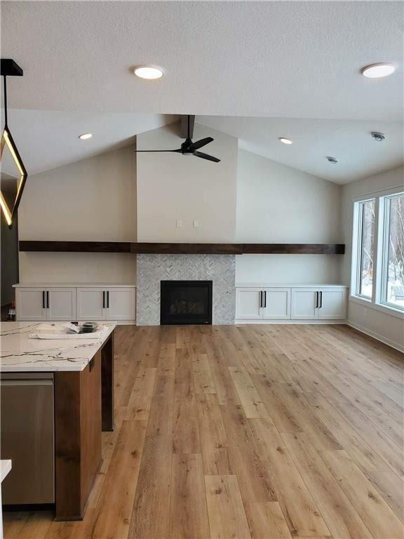 unfurnished living room featuring ceiling fan, light wood-type flooring, lofted ceiling, and a tiled fireplace