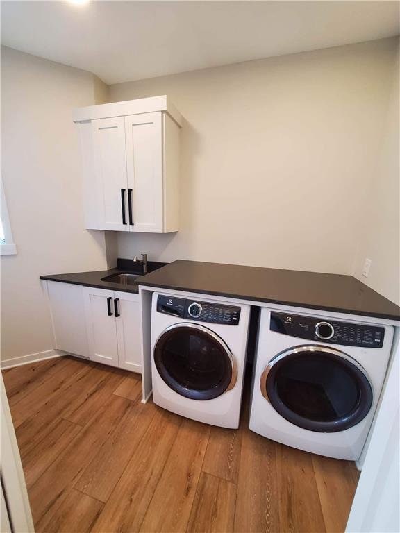 laundry room featuring cabinets, light wood-type flooring, washer and clothes dryer, and sink