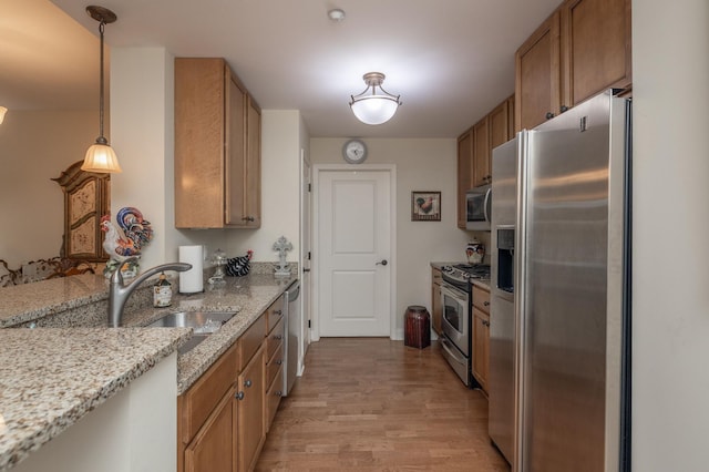 kitchen featuring light stone counters, light hardwood / wood-style flooring, sink, pendant lighting, and appliances with stainless steel finishes