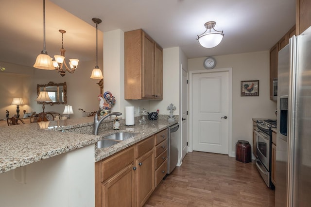 kitchen featuring light stone counters, stainless steel appliances, light wood-type flooring, pendant lighting, and sink