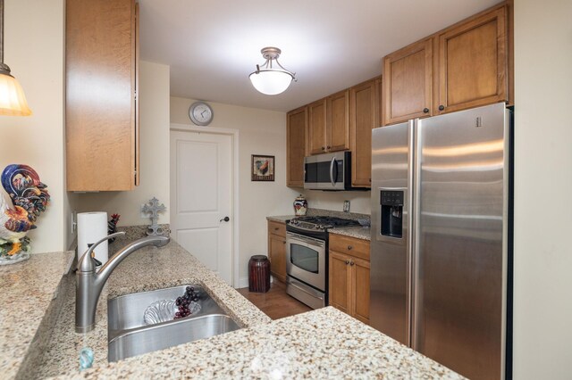 kitchen featuring light hardwood / wood-style floors, sink, light stone countertops, pendant lighting, and appliances with stainless steel finishes