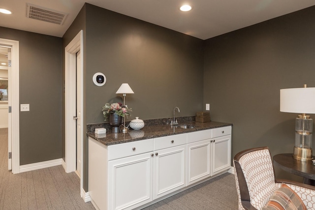 bar with white cabinetry, light carpet, sink, and dark stone countertops