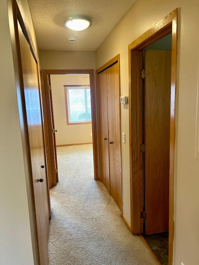 hall with a textured ceiling and light colored carpet