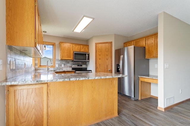 kitchen featuring appliances with stainless steel finishes, kitchen peninsula, dark wood-type flooring, decorative backsplash, and sink