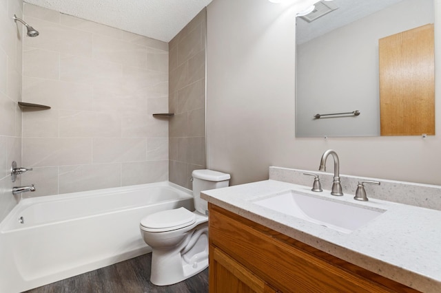 full bathroom with a textured ceiling, tiled shower / bath, hardwood / wood-style flooring, toilet, and vanity