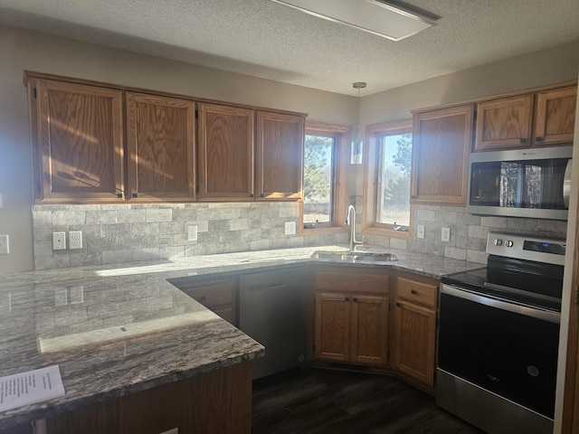 kitchen with appliances with stainless steel finishes, light stone countertops, a textured ceiling, sink, and decorative light fixtures