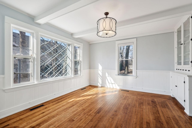 unfurnished dining area with plenty of natural light, wood-type flooring, and beam ceiling