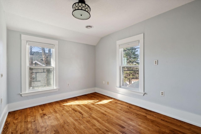 empty room with hardwood / wood-style floors, vaulted ceiling, and a healthy amount of sunlight