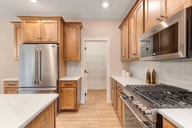 kitchen featuring light wood-type flooring, stainless steel appliances, brown cabinetry, decorative backsplash, and light stone countertops