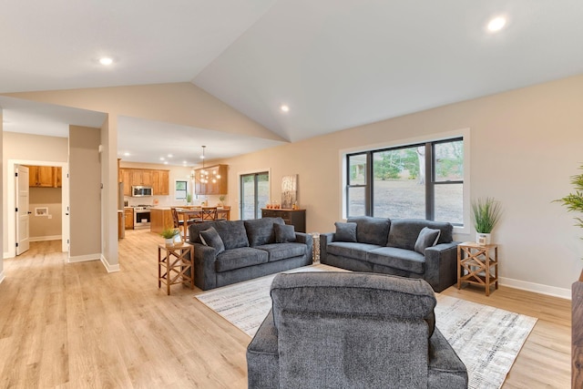 living room with light wood finished floors, a notable chandelier, a healthy amount of sunlight, and lofted ceiling