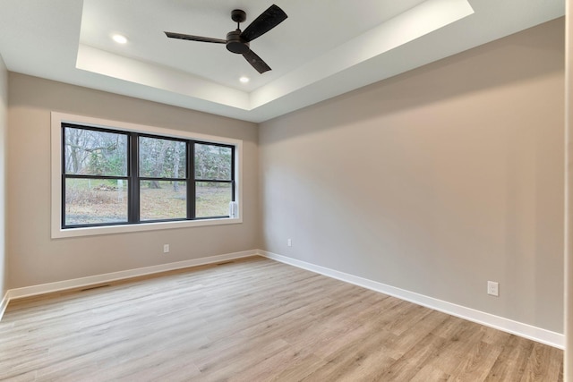 spare room featuring light wood-type flooring, a tray ceiling, baseboards, and a ceiling fan