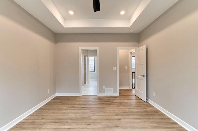 empty room featuring recessed lighting, baseboards, a tray ceiling, and light wood-style floors