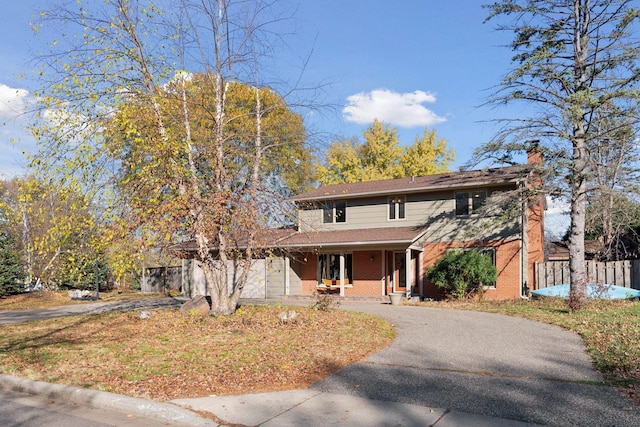 traditional-style home with brick siding, driveway, a chimney, and fence