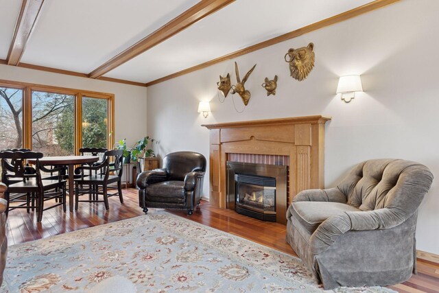 living room with a glass covered fireplace, beamed ceiling, wood finished floors, and ornamental molding