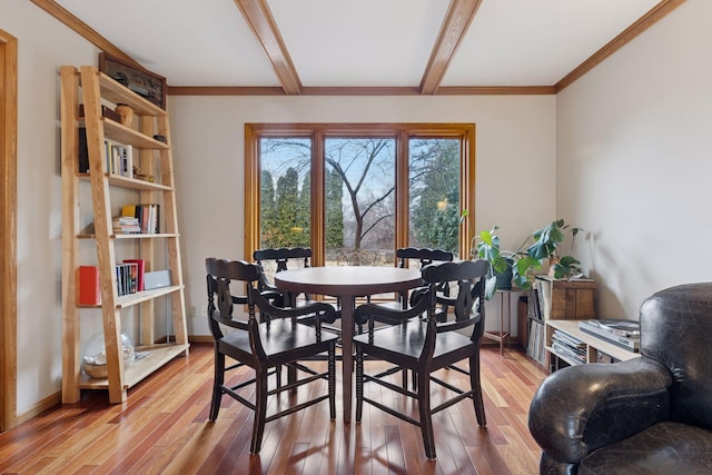 dining room featuring beam ceiling, light wood-style floors, baseboards, and ornamental molding