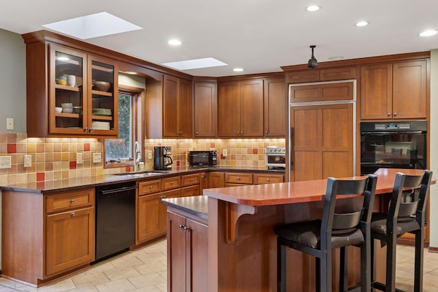 kitchen featuring a sink, black appliances, glass insert cabinets, a kitchen bar, and backsplash