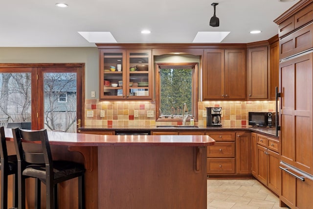 kitchen with glass insert cabinets, black microwave, a breakfast bar area, paneled built in fridge, and a skylight