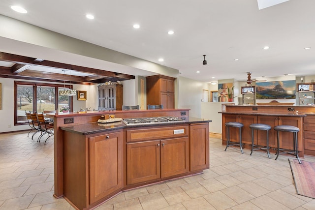 kitchen with a breakfast bar, recessed lighting, stainless steel gas stovetop, beamed ceiling, and a center island