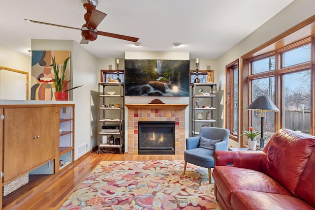 living area with visible vents, baseboards, ceiling fan, a tile fireplace, and wood finished floors