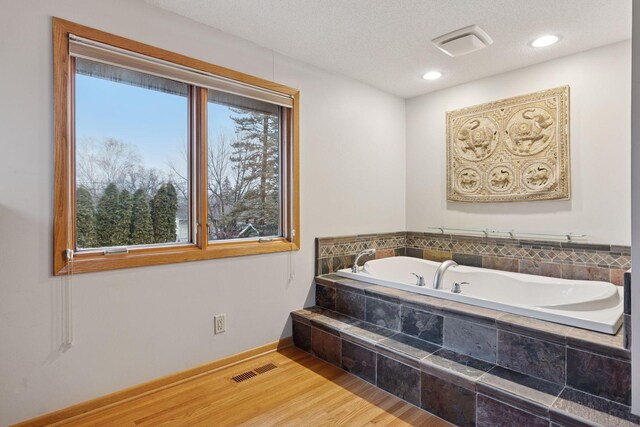 bathroom featuring a bath, wood finished floors, visible vents, and baseboards