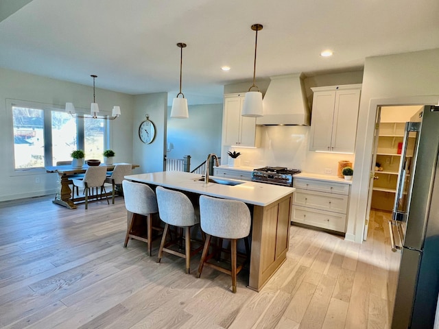 kitchen with sink, appliances with stainless steel finishes, a kitchen island with sink, custom range hood, and white cabinets