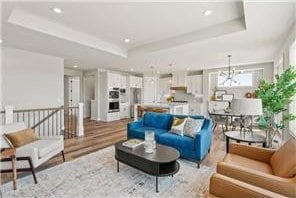 living room with light hardwood / wood-style floors, a raised ceiling, and an inviting chandelier