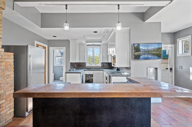 kitchen featuring decorative backsplash, stainless steel fridge, brick wall, pendant lighting, and white cabinets