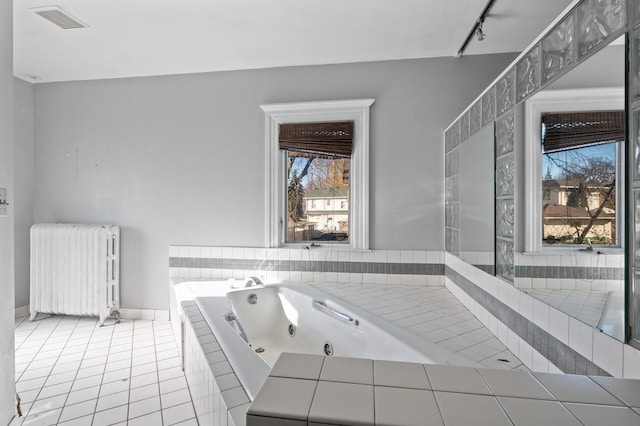 bathroom featuring tile patterned flooring, a relaxing tiled tub, rail lighting, and radiator