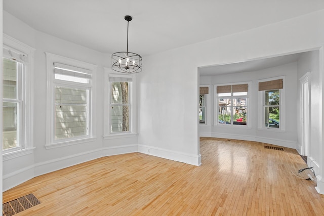 unfurnished dining area featuring light wood-type flooring and an inviting chandelier