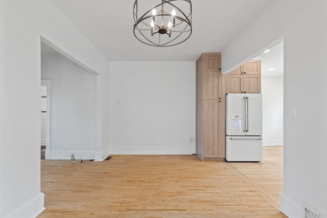 kitchen with a notable chandelier, white fridge with ice dispenser, light brown cabinets, light wood-type flooring, and decorative light fixtures